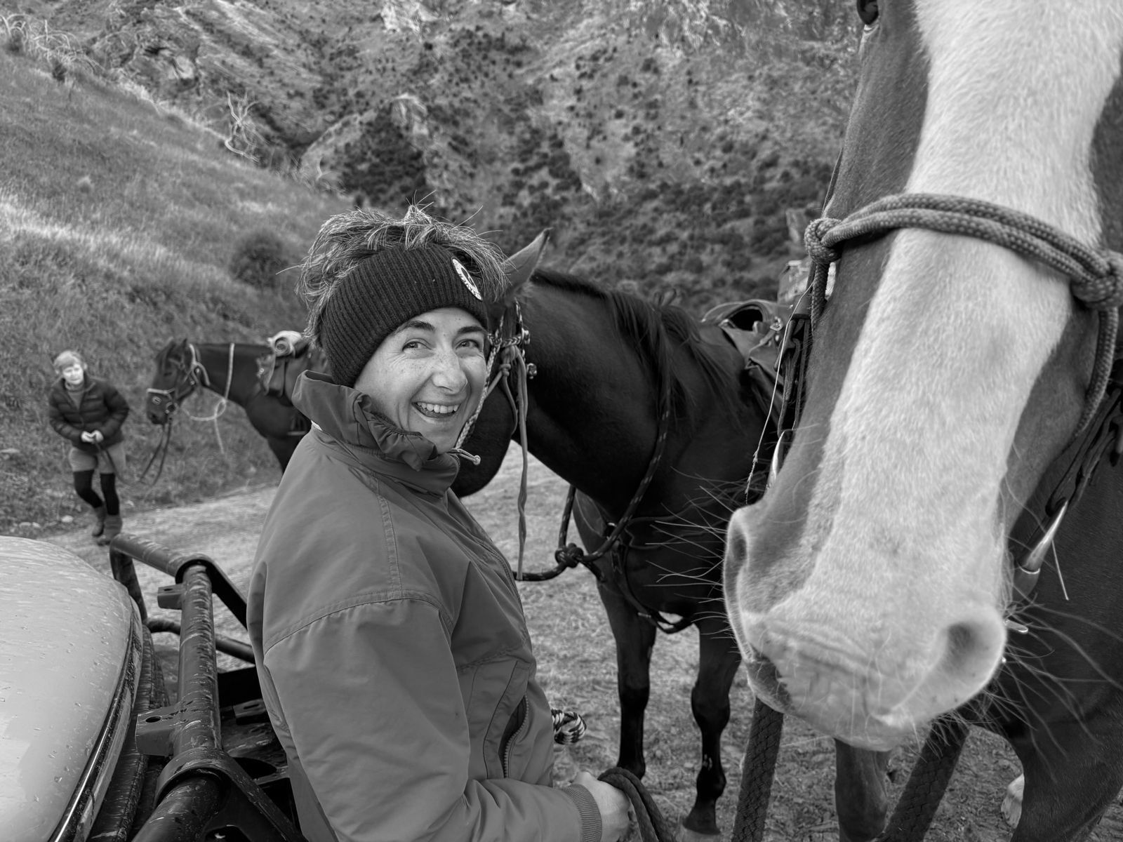 Poppie Johnson in a beanie beside saddled horses on a station track, with a white-blazed horse in the foreground